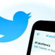 A phone with #FakeNews written in the search bar with the Twitter bird logo in the background.